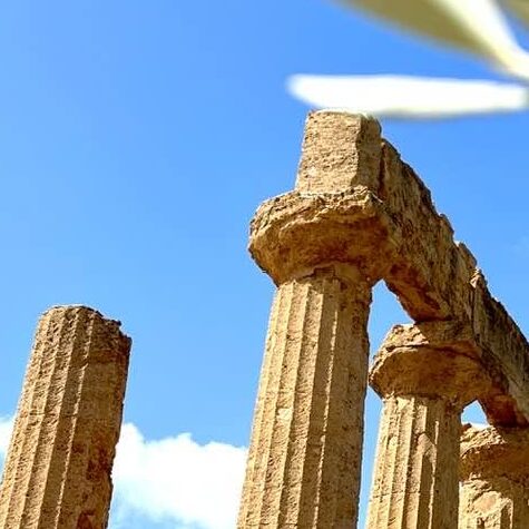 Close-up of ancient Greek stone columns at the Valley of the Temples in Agrigento, Sicily, against a pink and purple sunset sky.