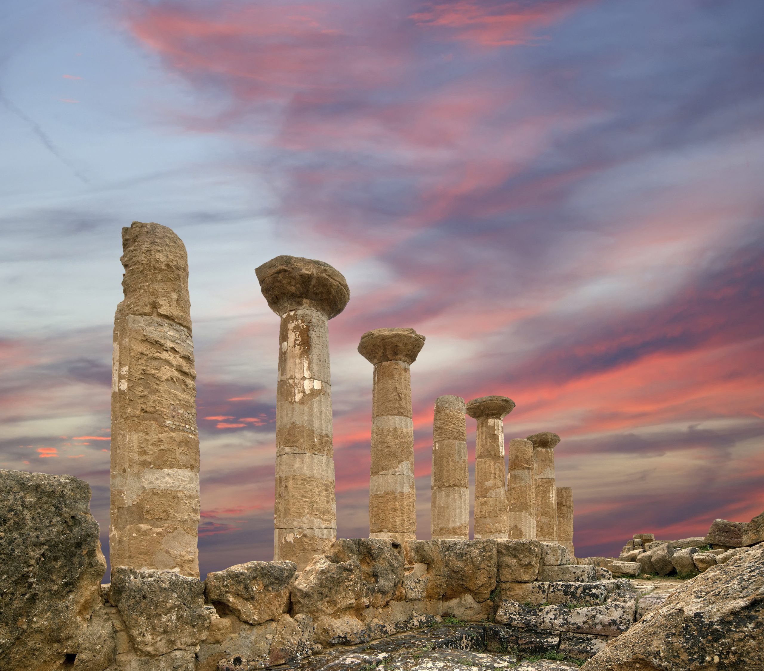 Ancient Greek columns in the Valley of the Temples, Agrigento, Sicily, beneath a pink and purple sunset sky.